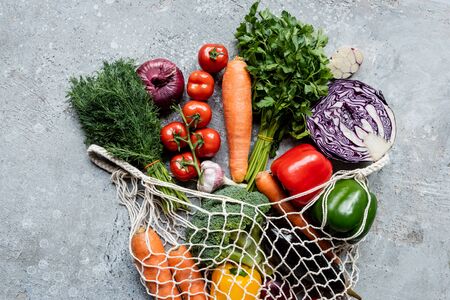 top view of fresh ripe vegetables in string bag on grey concrete surfaceの写真素材
