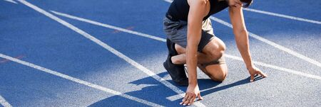 partial view of handsome runner in start position on running track at stadium, panoramic shot