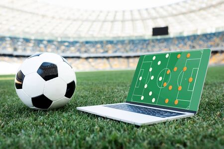 soccer ball and laptop with formation on screen on grassy football pitch at stadiumの写真素材