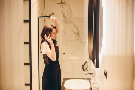 happy woman in black dress talking on smartphone and holding medical mask, end of quarantine conceptの写真素材