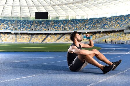 handsome sportsman resting and drinking water on running track at stadiumの写真素材