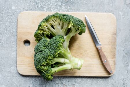 top view of fresh green cut broccoli on wooden cutting board with knife on grey surfaceの写真素材