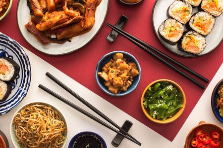 top view of chopsticks near korean topokki and traditional side dishes on white and crimsonの写真素材