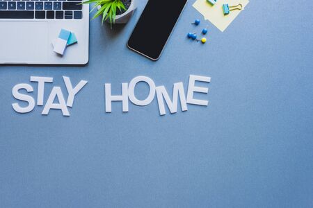 Top view of lettering stay home near digital devices, stationery and plant on blue surfaceの写真素材