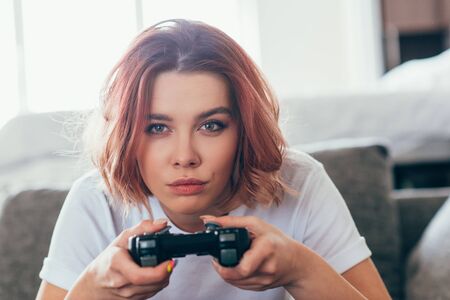 KYIV, UKRAINE - APRIL 15, 2020: concentrated girl playing video game with joystick at home on self isolationの写真素材