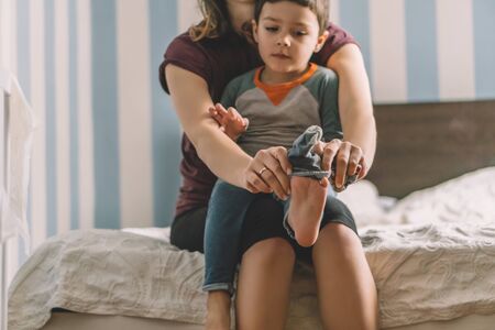 cropped view of woman dressing adorable son while sitting on bedの写真素材