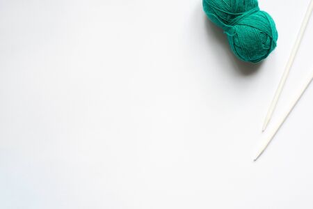 top view of green wool yarn and knitting needles on white background