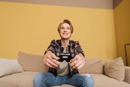KYIV, UKRAINE - APRIL 24, 2020: selective focus of cheerful man holding joystick while playing video game in living roomの写真素材
