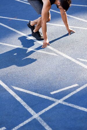 cropped view of handsome runner in start position on running track at stadium