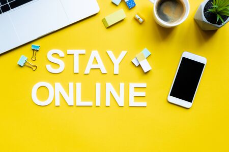 Top view of stay online lettering near digital devices, cup of coffee and stationery on yellow surfaceの写真素材