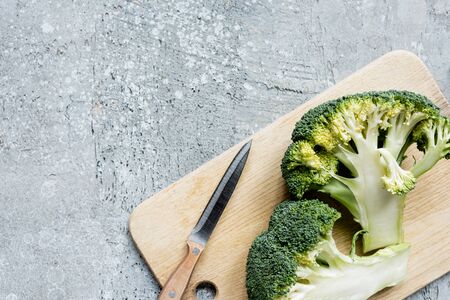 top view of fresh green cut broccoli on wooden cutting board with knife on grey surfaceの写真素材