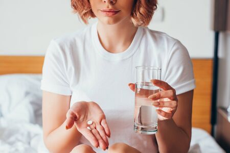 cropped view of girl holding pill and glass of water at home on self isolationの写真素材