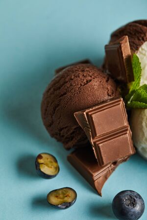 close up view of tasty brown ice cream with berries, chocolate and mint on blue backgroundの写真素材