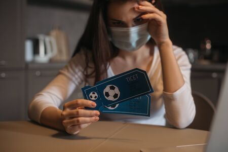 selective focus of upset woman in medical mask holding sport match tickets at homeの写真素材