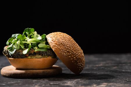 tasty vegan burger with microgreens served on wooden board isolated on blackの写真素材