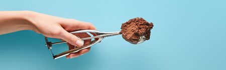 cropped view of woman holding scoop with chocolate ice cream on blue background, panoramic shotの写真素材