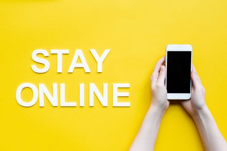 Top view of woman holding smartphone near stay online lettering on yellow backgroundの写真素材