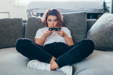 KYIV, UKRAINE - APRIL 15, 2020: focused girl playing video game with joystick at home on self isolationの写真素材