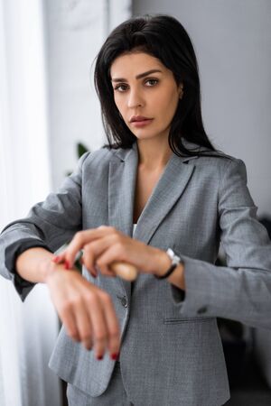 selective focus of businesswoman applying makeup foundation on hand with bruise and looking at camera, domestic violence conceptの写真素材