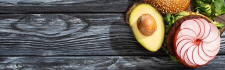 top view of tasty vegan burger with microgreens, radish, tomato and avocado on cutting board served on wooden table, panoramic cropの写真素材