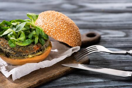 tasty vegan burger with microgreens served on cutting board with cutlery on wooden tableの写真素材