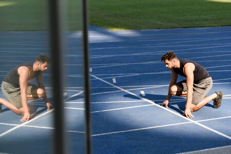 selective focus of handsome runner in start position on running track at stadium