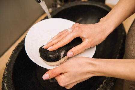 cropped view of woman washing white plate with spongeの写真素材