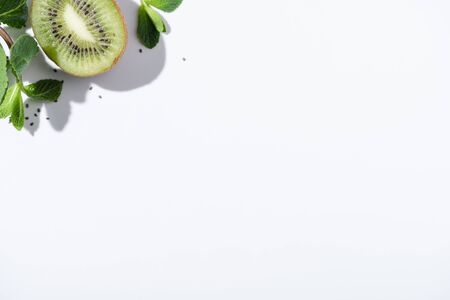 top view of green peppermint near fresh kiwi fruit and black seeds on whiteの写真素材