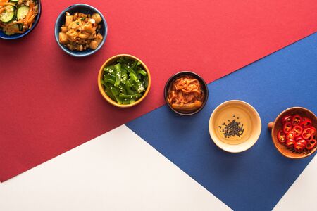 top view of bowls with korean side dishes and oil on blue, crimson and whiteの写真素材