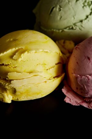 close up view of delicious yellow, pink and green ice cream balls isolated on blackの写真素材