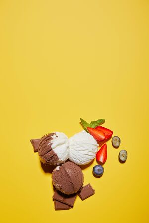 top view of tasty brown and white ice cream with berries, chocolate and mint on yellow backgroundの写真素材