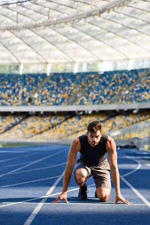 handsome runner in start position on running track at stadiumの写真素材