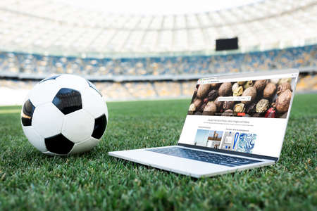 KYIV, UKRAINE - JUNE 20, 2019: soccer ball and laptop with depositphotos website on grassy football...