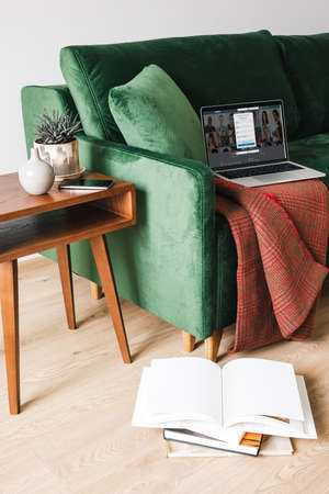 KYIV, UKRAINE - APRIL 14, 2020: green sofa with blanket and laptop with LinkedIn website near wooden coffee table with plant and smartphone near books on floorのeditorial素材