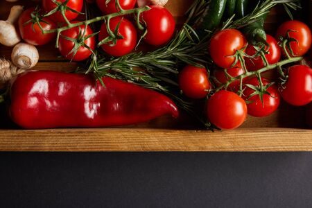 top view of cherry tomatoes, mushrooms near rosemary and red chili pepper in wooden box on blackの写真素材