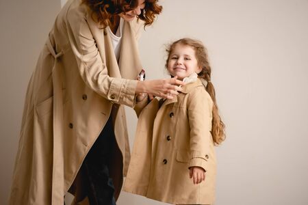 happy mother touching trench coat on cheerful kidの写真素材