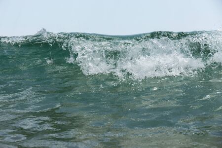 Close up view of sea wave with foam and blue sky at background