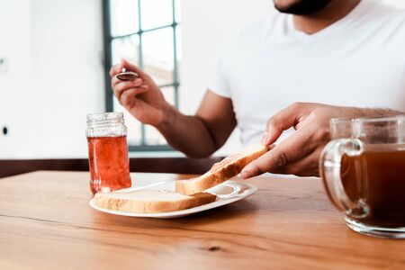 cropped view of african american man holding spoon near jar with sweet jam and toast bread on plateの写真素材