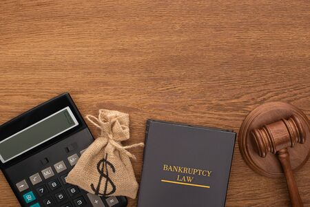 top view of bankruptcy law book, money bag, calculator and gavel on wooden background