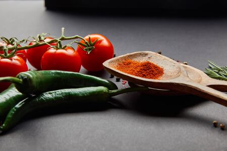 organic cherry tomatoes, rosemary, peppercorns, wooden spoons with paprika powder and green chili peppers on blackの写真素材