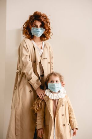 curly mother and daughter in medical masks standing in trench coatsの写真素材