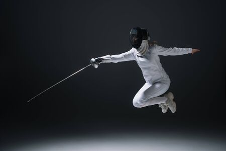 Fencer holding rapier while jumping isolated on blackの写真素材