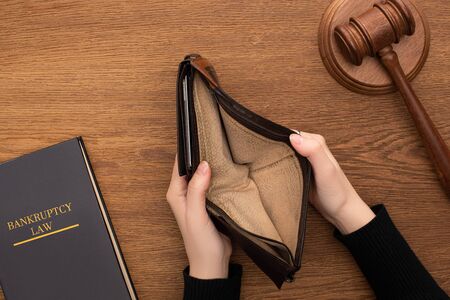 top view of female hands with empty wallet, bankruptcy law book and gavel on wooden background