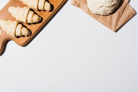 top view of fresh croissants on wooden cutting board near raw dough on white backgroundの写真素材