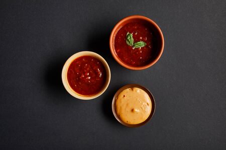 top view of bowls with tomato and mustard sauces on blackの写真素材