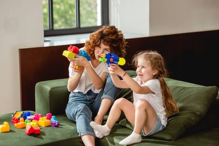 curly mother and daughter with water gun playing in living roomの写真素材