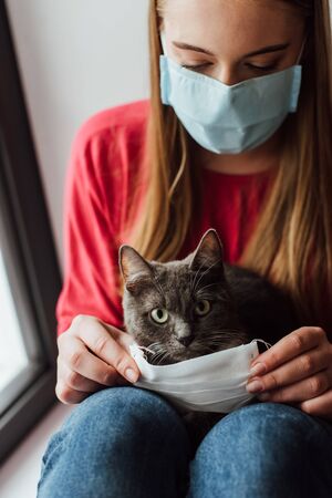 young woman in medical mask sitting with cute catの写真素材