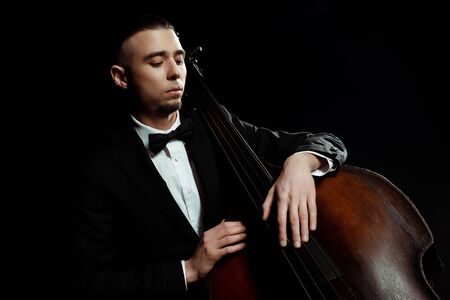 young musician playing on double bass isolated on blackの写真素材