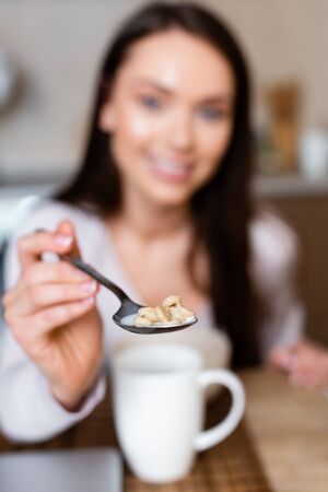 selective focus of cheerful girl holding spoon with tasty corn flakes with milkの写真素材