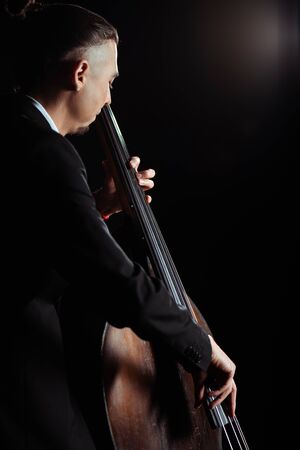 professional young musician playing on contrabass on dark stageの写真素材